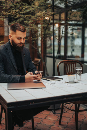 Young bearded businessman using a smartphone while working in a cafeの写真素材