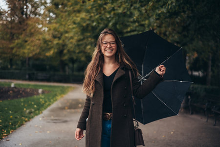Beautiful young woman holding an umbrella while out in the city on a rainy dayの写真素材
