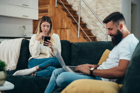 Shot of a young couple using their digital devices while sitting on a couch at homeの写真素材