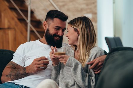 Young beautiful couple drinking coffee in the morning while relaxing at home and being romanticの写真素材