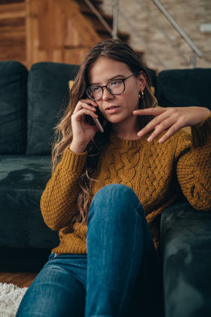 Shot of an attractive young woman sitting on her living room floor and using smartphone at homeの写真素材