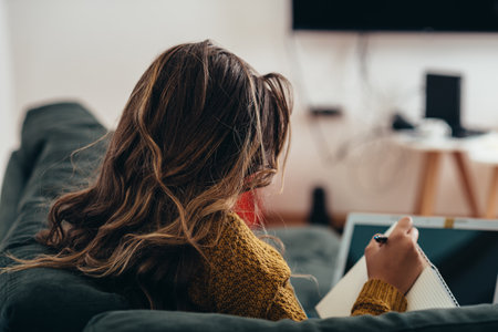 Shot of a young woman using her laptop and a notebook at homeの写真素材