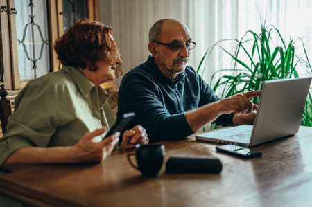 Senior couple using a laptop and a smartphone while sitting in the office at home