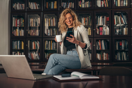 Young businesswoman using a smartphone while drinking coffee on her break in the office