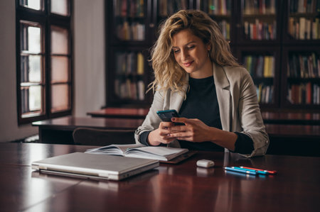 Young beautiful blonde businesswoman using a smartphone while working in the officeの写真素材