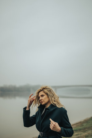 Young blonde woman standing near the river in a green coatの写真素材