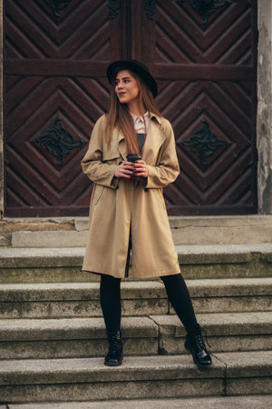 Beautiful stylish woman drinking coffee takeaway while posing in front of the wooden doorの写真素材