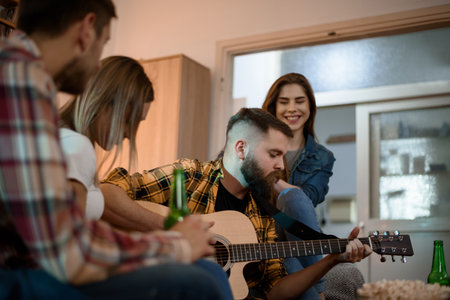 A group of friends on a house party playing guitar and drinking beer while having funの写真素材