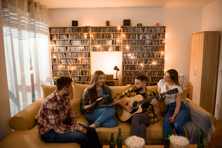 Group of friends on a house party playing guitar and drinking beer while having fun all together on...