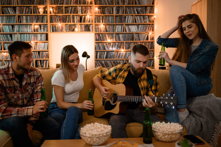 Group of friends on a house party playing guitar and enjoying music while having fun at home and drinking beerの写真素材