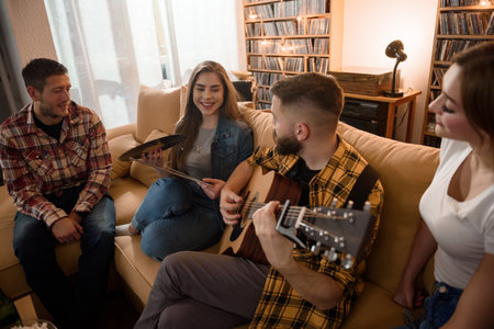 Group of friends on a house party playing guitar and enjoying music while having fun at homeの写真素材