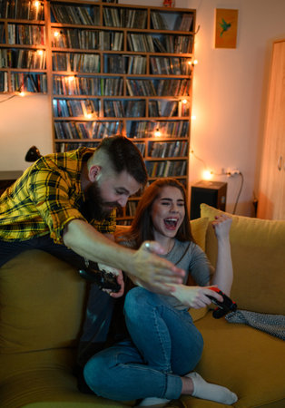 Couple playing video games and holding consoles while sitting on the couch at home and being...