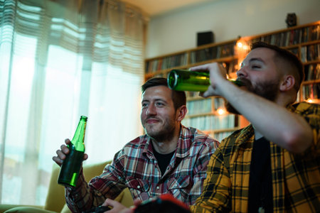Two best friends playing video games while relaxing at home on the couch and drinking beerの写真素材