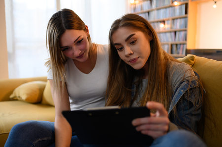Young students studying for their exam together at home while sitting on the yellow sofa