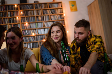Group of friends on a house party drinking beer and eating pizza while hanging together and having...
