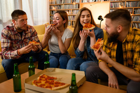 Young group of friends on a house party having fun while eating pizza and drinking beerの写真素材