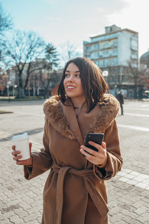 Shot of a young hispanic businesswoman out in the city while using smartphone and a coffee takeawayの写真素材
