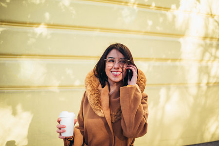 Young hispanic woman using a smartphone and a coffee takeaway while out in the cityの写真素材