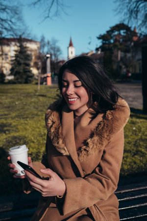 Shot of a hispanic young businesswomen using a smartphone and drinking coffee takeaway while walking through the cityの写真素材