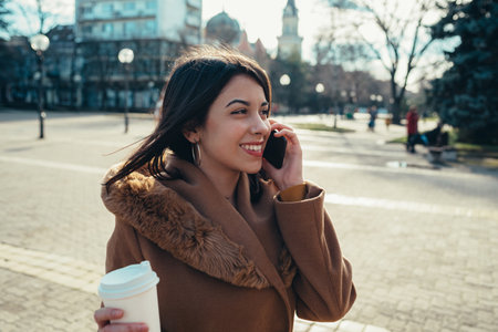 Shot of an attractive hispanic young woman on a call while drinking coffee takeawayの写真素材
