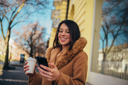 Young hispanic woman using a smartphone and a coffee takeaway while out in the cityの写真素材