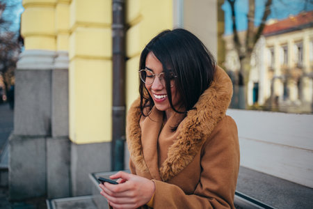 Young hispanic woman using smartphone while out in the city wearing coatの写真素材