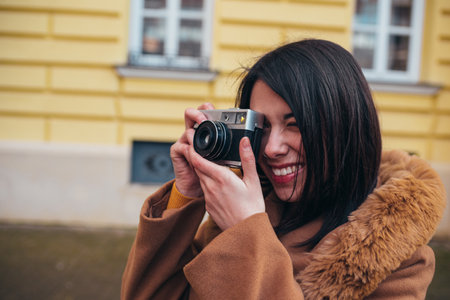 Young hispanic woman using a retro camera while out in the city wearing coat