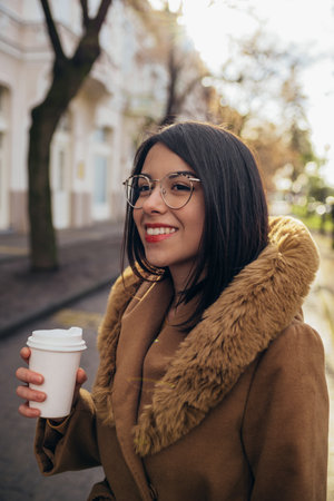 Young hispanic woman drinking coffee takeaway while out in the city wearing coatの写真素材