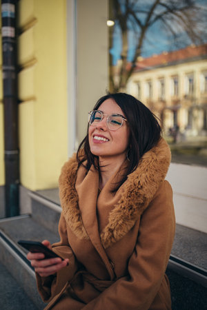 Young hispanic woman using smartphone while out in the city wearing coatの写真素材