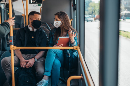 Young couple wearing protective masks riding a bus and talking to each otherの写真素材