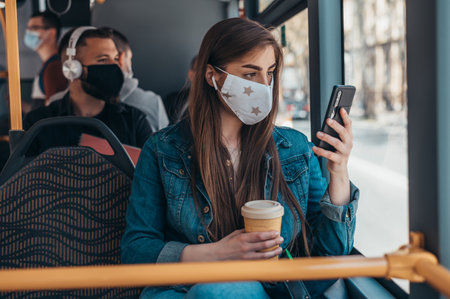 Young woman wearing protective mask and using smartphone while riding a bus during a covid19 pandemicの写真素材