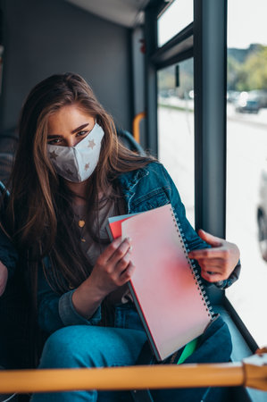 Woman wearing protective mask while riding a bus and sitting on a distance from other passengers due to covid19 pandemicの写真素材