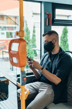 Young man wearing protective mask and using a smartphone while riding a bus due to a corona virus pandemicの写真素材