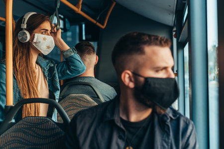 Young man wearing a protective mask while riding the bus while sitting on a distance from other passengers due to corona virus pandemicの写真素材