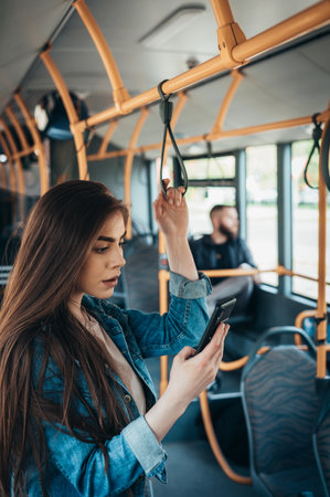 Young woman using a smartphone and standing while riding the busの写真素材