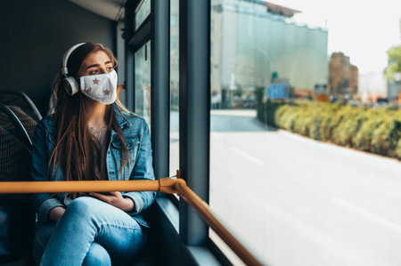 Woman wearing a sterile protective mask while riding in a public bus while looking on a streetの写真素材