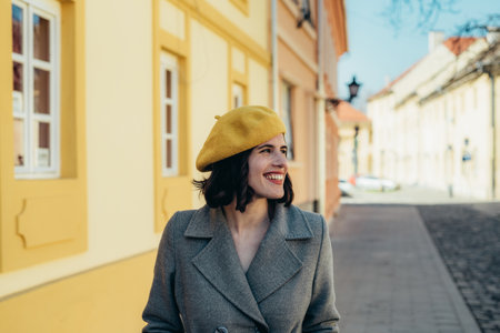Beautiful young woman wearing yellow beret and a gray coat walking down the city streetsの写真素材