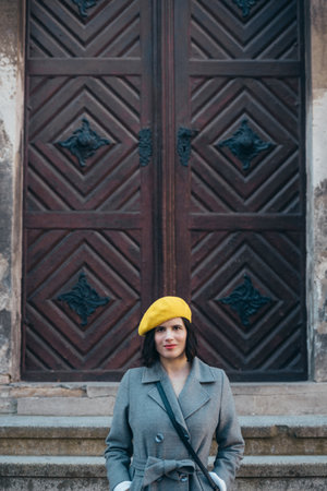 Shot of an attractive young woman wearing gray coat and a yellow beret while standing in front of a wooden doorsの写真素材