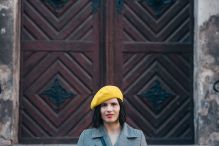 Beautiful young woman wearing yellow beret and a gray coat walking down the city streets
