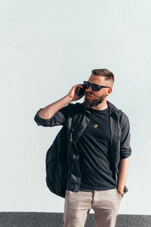 Young handsome man using a smartphone dressed casual while standing in front of a white background outside on a sunny dayの写真素材