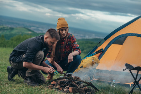 Couple of campers lighting the camp fire while spending their weekend together in the natureの写真素材