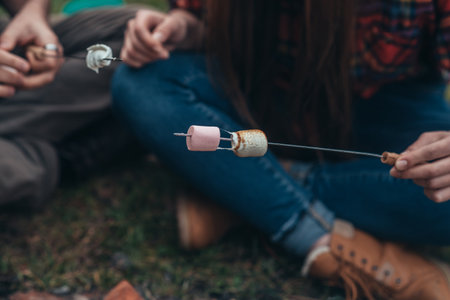Unrecognized woman holding a marshmallows on a stick above fire while camping in the nature and having funの写真素材