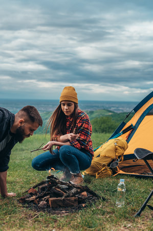 Couple of campers lighting a fire while near the tent during their weekend in th natureの写真素材