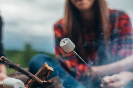 Unrecognizable campers holding marshmallows on a stick above the camp fire in a natureの写真素材
