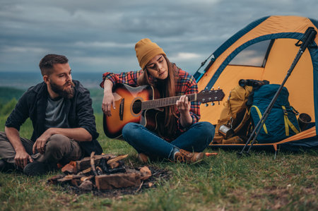 Couple of campers playing guitar while sitting near the tent and spending romantic weekend in the...