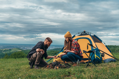 Couple of campers lighting a fire near the tent in a camp while spending weekend in the natureの写真素材