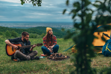 Couple of campers playing guitar and sitting near the tent while camping in the natureの写真素材