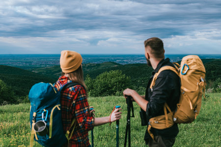 A young couple of hikers using trekking poles and wearing backpacks with camping gear while spending time in natureの写真素材