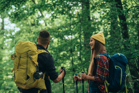 A young couple of hikers using trekking poles and wearing backpacks with camping gear while spending...