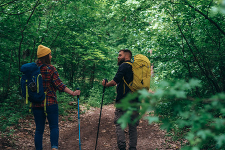 Couple of hikers using trekking poles and wearing backpacks with camping gear while out in the...
